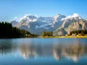 Alpenmeer met spiegeling van besneeuwde bergen en een dorpje aan de oever.