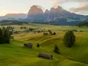 Groene alpenweide met verspreide houten schuren en bergtoppen op de achtergrond.