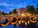 Verlichte grachtenpanden en een boogbrug over een Amsterdamse gracht in de avondschemering.