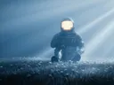 Een astronaut knielt in een veld met kleine witte bloemen terwijl licht door mist schijnt.