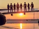 Silhouetten van acht personen die hand in hand op een vliegtuigvleugel staan bij zonsondergang.