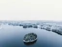 Luchtfoto van een besneeuwd eilandje met bomen in een meer, omgeven door besneeuwd bos