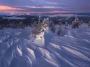 Besneeuwde bergtop met windpatronen in sneeuw bij een kleurrijke zonsondergang.
