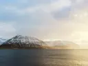 Besneeuwde bergen aan het water bij zonsopkomst met lichte nevel.