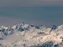Panorama van besneeuwde bergtoppen tegen een grijsblauwe lucht.