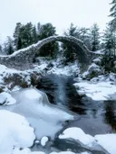 Oude stenen boogbrug over een gedeeltelijk bevroren beek met sneeuw op de oevers