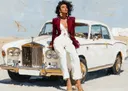 Olieverfportret van een vrouw in bordeauxrode blazer zittend op een witte klassieke luxeauto in een woestijnlandschap