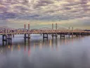 Een lange stalen brug over een rivier onder een bewolkte lucht bij schemering.