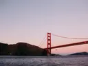 De rode pijler van de Golden Gate Bridge met steile heuvels en een vogel in de lucht bij schemering.