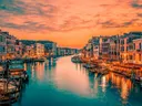 Venetiaans kanaal met historische gebouwen en bootjes onder een oranje avondlucht.