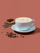Kopje cappuccino met latte-art naast koffiebonen en lavendel op een terracotta achtergrond