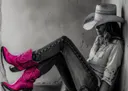 Zwart-wit foto van een vrouw met cowboyhoed en felroze cowboylaarzen