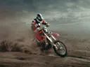 Motorcrossrijder in rood-zwarte outfit rijdt door opstuivend stof.