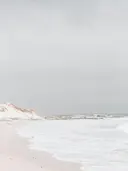 Foto van duinen en een bewolkte zee met rotsen op de achtergrond