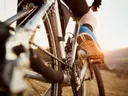 Close-up van een fietser die trapt, met de ketting en het achterwiel van de fiets in beeld bij zonsondergang.