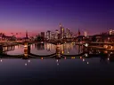 Skyline van Frankfurt met verlichte wolkenkrabbers en een brug die weerspiegelt in de rivier bij avondschemering.
