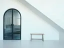 Wit minimalistisch interieur met een gewelfde glazen deur en een houten bankje