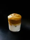 Glas met gelaagde koffie en melkschuim tegen een zwarte achtergrond.