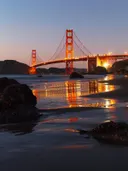 Golden Gate Bridge verlicht bij schemering met reflecties op een strand.