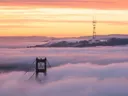Bovenkant van de Golden Gate Bridge boven een mistlaag bij zonsopkomst