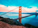 Uitzicht vanaf een begroeide heuvel op de Golden Gate Bridge met de skyline van San Francisco op de achtergrond bij schemering.