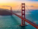 De Golden Gate Bridge in San Francisco bij zonsondergang, met een oranje en roze gekleurde lucht boven de baai.