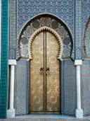 Gouden versierde deur met geometrisch patroon, omgeven door blauw-groene mozaïektegels en witte zuilen.
