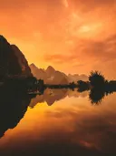 Karstbergen bij zonsondergang met spiegelend water in oranje en gouden tinten.