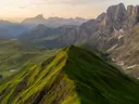 Luchtfoto van een groene bergkam met rotsachtige bergtoppen op de achtergrond bij zonsopkomst.