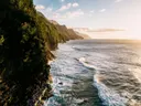 Steile, groen begroeide kliffen langs de kust met brekende golven bij zonsondergang.