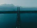 Grote hangbrug over een brede rivier bij avondschemering met een stad op de achtergrond.