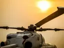 Close-up van de rotor en cockpit van een helikopter tegen een oranje zonsondergang.