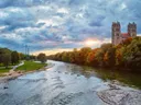 Rivier omgeven door herfstbomen met kerktorens op de achtergrond bij zonsondergang.