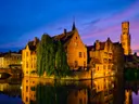Verlichte historische gebouwen aan een kanaal in de schemering.