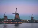 Drie Hollandse windmolens aan het water tijdens de schemering met een zeilboot