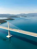 Een luchtfoto van een moderne kabelbrug over een turquoise baai met eilanden op de achtergrond.