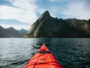 Uitzicht vanuit een kajak over water naar een steile bergtop in een fjord.