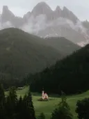 Kleine kapel in een groen dal onder mistige bergpieken.