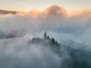 Kerktoren op een eiland die boven de mist uitsteekt bij zonsopkomst.