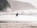Foto van een kind dat met een bodyboard langs de branding rent bij hoge kliffen