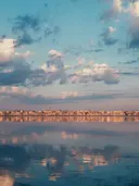 Skyline van een kustplaats weerspiegeld in kalm water bij schemering.
