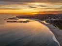 Luchtfoto van een kuststad met jachthaven, strand en zee bij zonsondergang.