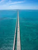 Luchtfoto van een lange rechte brug die over helder turquoise zeewater loopt.