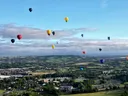 Meerdere gekleurde luchtballonnen zweven boven een groen landschap met dorpen.
