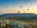 Luchtballonnen die opstijgen boven een landschap met rotsformaties bij zonsopkomst.