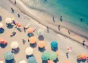 Foto-achtig schilderij van bovenaf van een strand met kleurrijke parasols en badgasten
