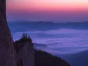Uitzicht vanaf een rots over een met mist gevulde bergvallei bij zonsondergang.