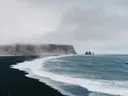Foto van mistige kliffen en rotsformaties bij een zwart zandstrand