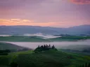 Mistige heuvels in Toscane bij zonsopkomst met een boerderij op een heuveltop