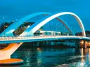 Verlichte moderne boogbrug over een rivier bij nacht met een passerende tram.